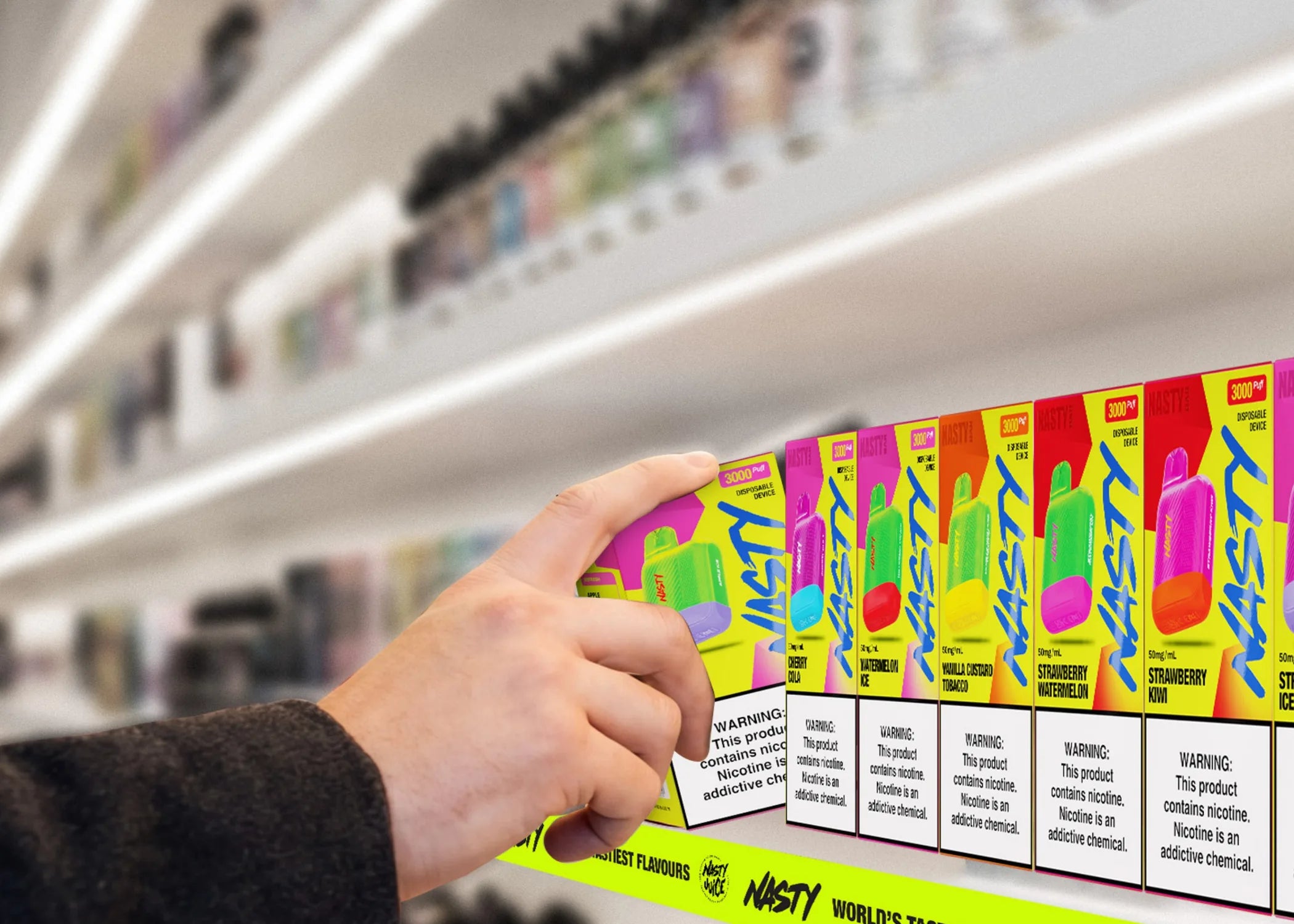 A hand lifting a NASTY BAR DX3K pack from a lit shelf of NASTY packs in a vape shop.